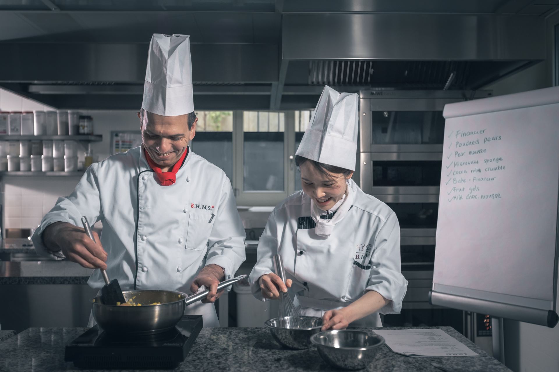 BHMS chef instructor and student prepare pastry components beside a flipchart production plan