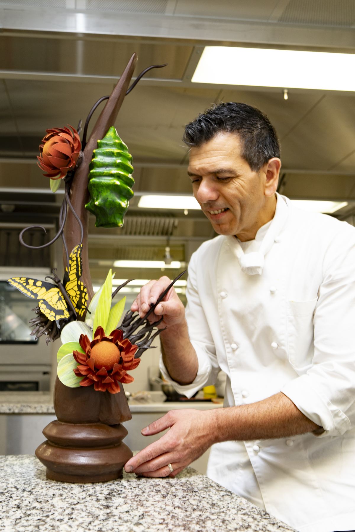 Chef adjusting a tall chocolate showpiece with coloured flowers and a yellow butterfly