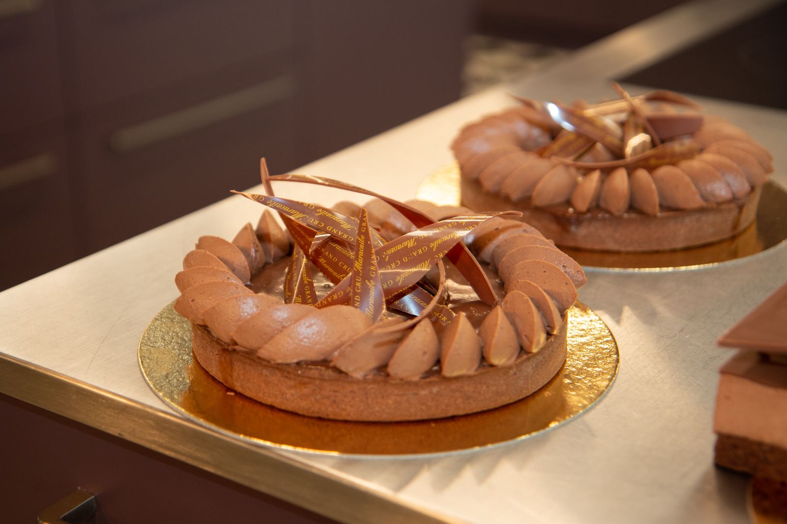 Two chocolate tarts on gold boards with piped chocolate teardrops and curved chocolate decorations