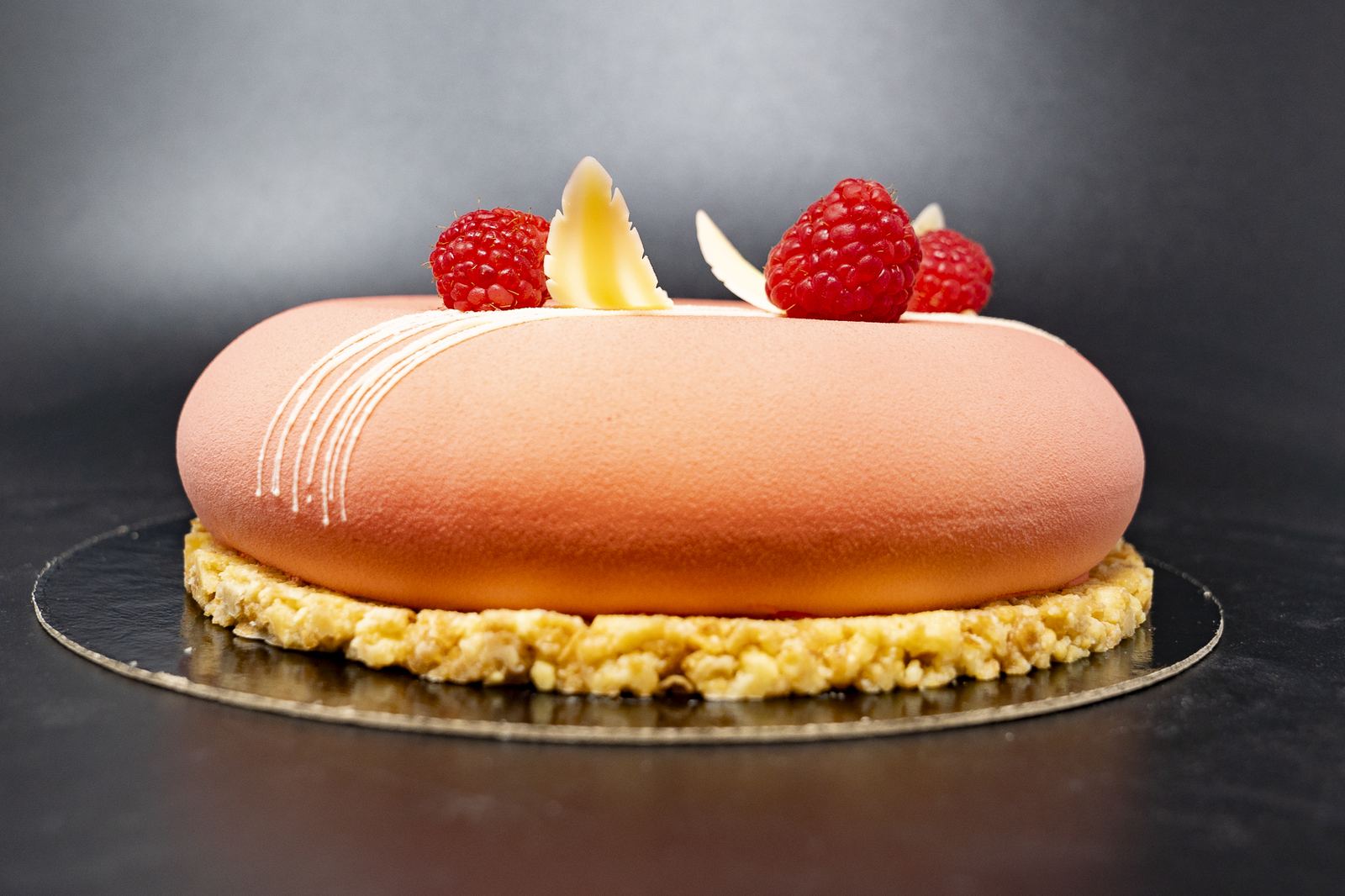 Round peach velvet-sprayed entremet topped with raspberries and white chocolate curls