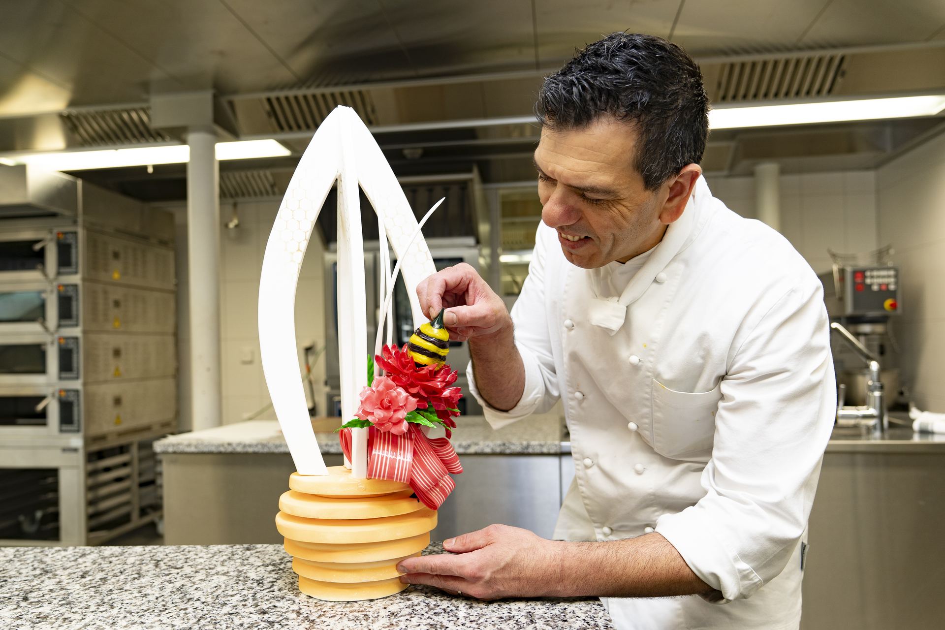Pastry chef places a sugar bee onto a tall honeycomb-themed sugar showpiece
