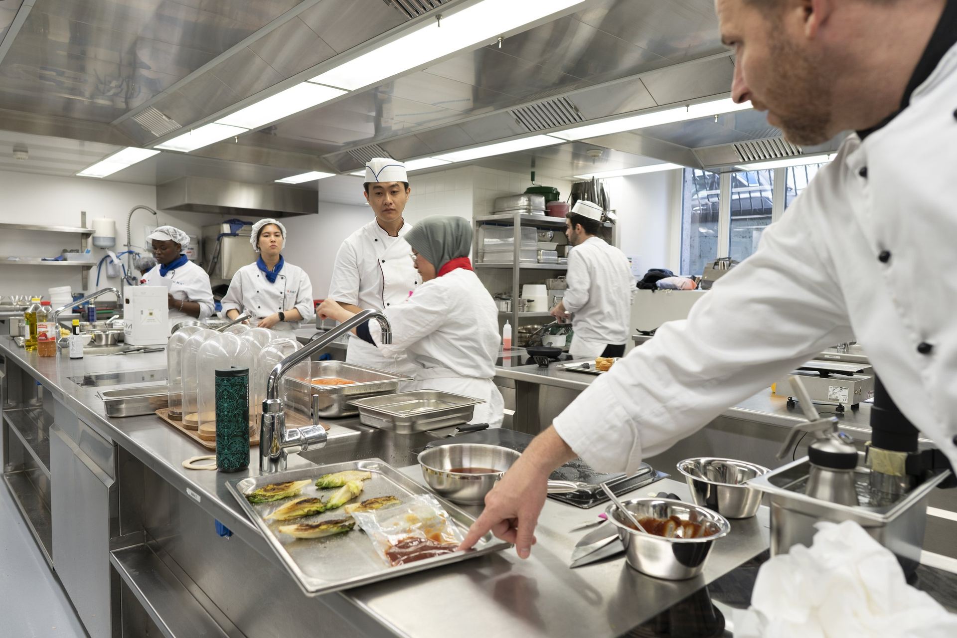 Wide view of a BHMS teaching kitchen with students at individual stations